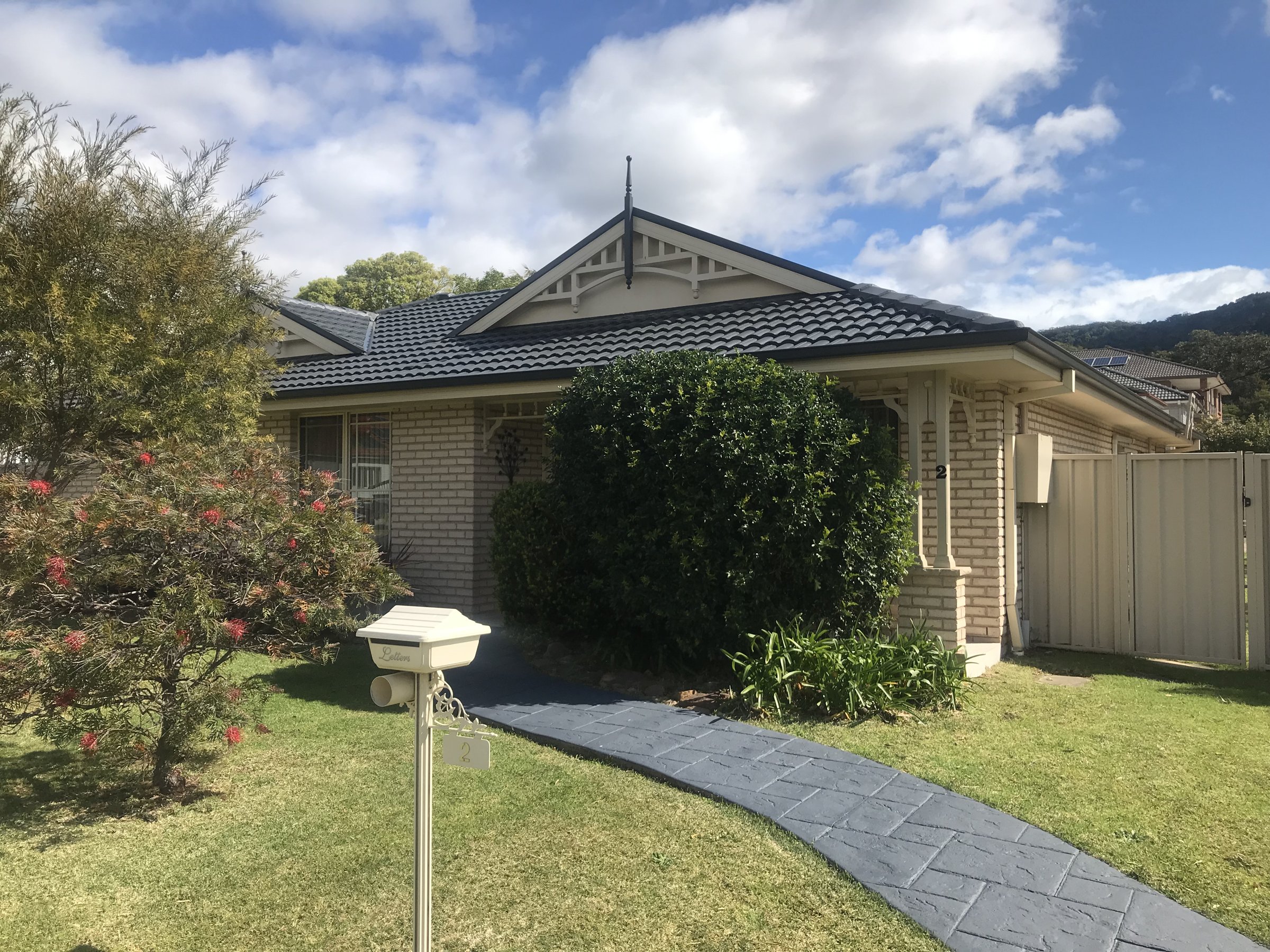 Cream brick home with a newly coated charcoal roof and decorative gable, escarpment behind